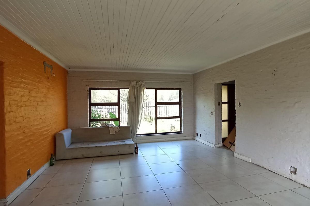 Spacious living area featuring tiled flooring, large windows for natural light, and a unique textured wall finish, offering a blank canvas for renovation.