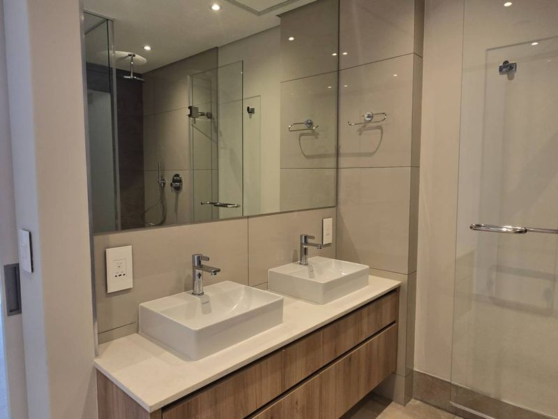 Modern bathroom featuring a double vanity with vessel sinks, large mirror, and a glass-enclosed shower, with direct access to a private balcony.