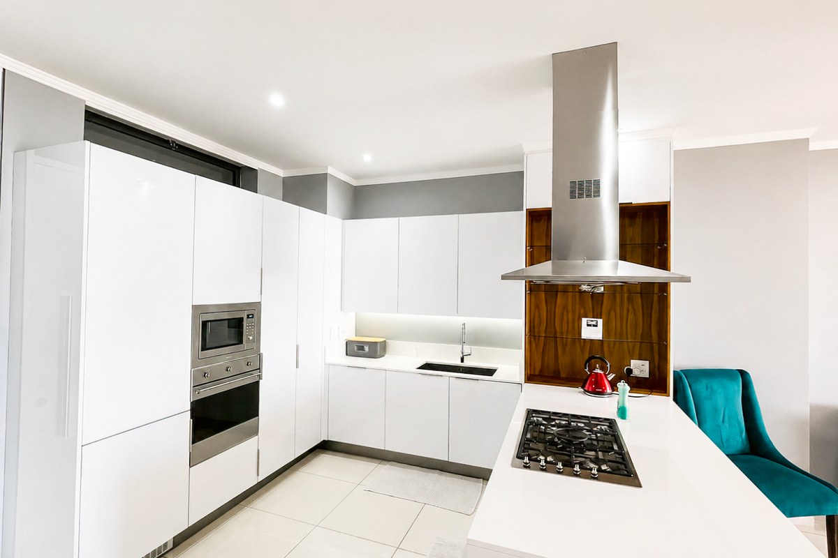 Modern kitchen featuring white gloss cabinetry, stone countertops, integrated appliances, gas hob, and a stainless steel extractor fan.