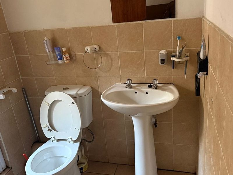 A compact bathroom featuring a pedestal washbasin, dual flush toilet, and neutral ceramic wall and floor tiling.