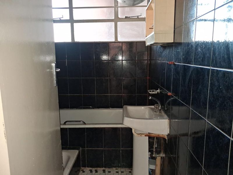 A dated bathroom featuring dark wall tiles, a pedestal basin, and a bathtub, requiring renovation to modernize the space.