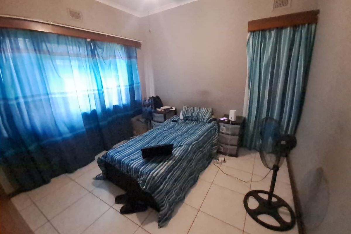 A bedroom featuring tiled flooring, ceiling cornices, and large windows with curtain rails.