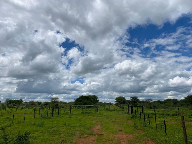 A view of the property entrance featuring a metal farm gate and wire fencing set within a natural, open landscape.