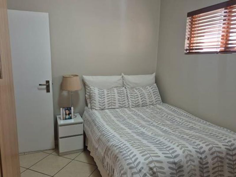 A compact bedroom featuring tiled flooring, a built-in wardrobe, and a window fitted with wooden venetian blinds.