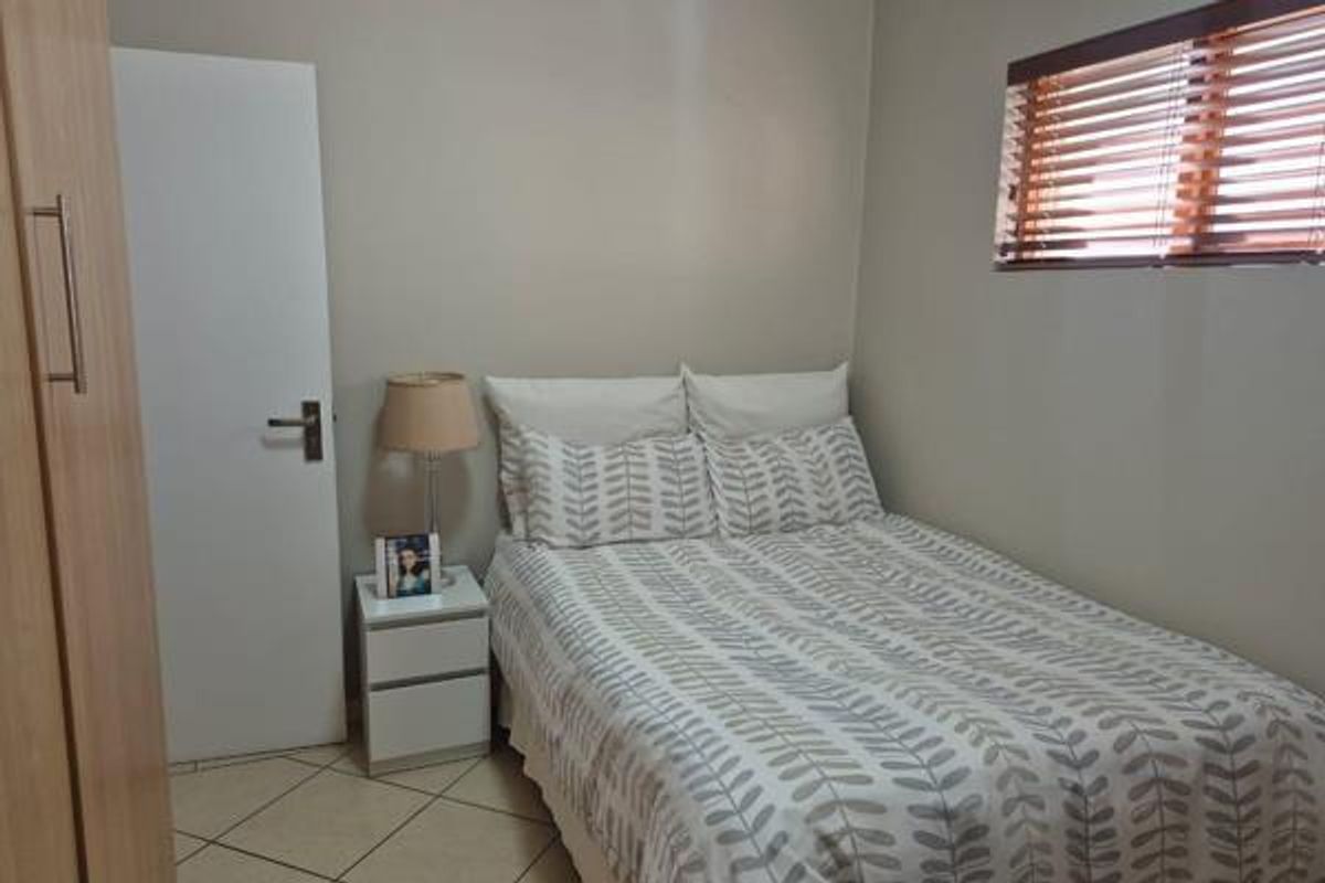 A compact bedroom featuring tiled flooring, a built-in wardrobe, and a window fitted with wooden venetian blinds.