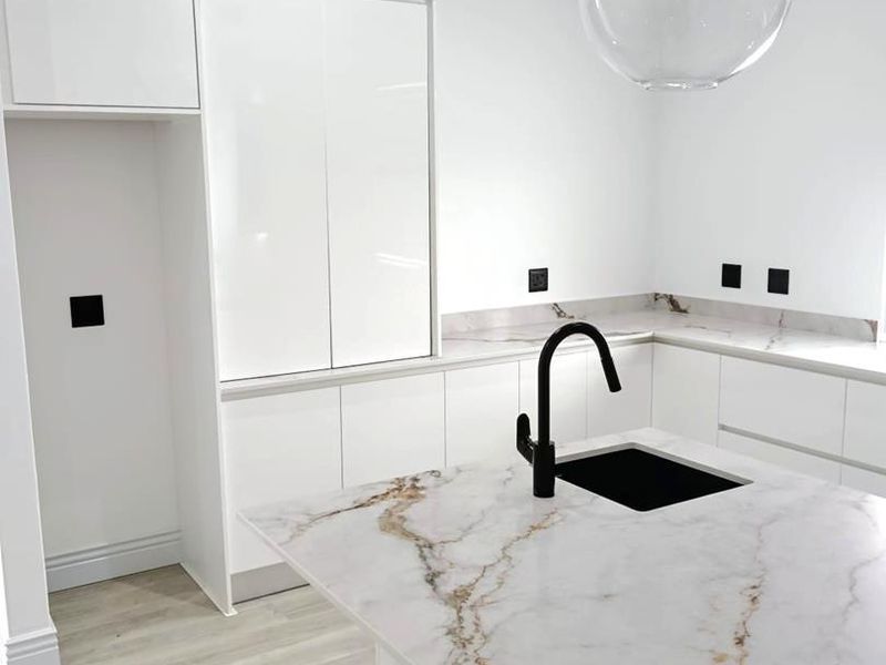 Modern kitchen featuring sleek white cabinetry, marble-look stone countertops, a black faucet, and contemporary pendant lighting in a clean, minimalist design.