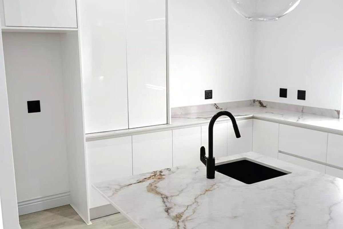 Modern kitchen featuring sleek white cabinetry, marble-look stone countertops, a black faucet, and contemporary pendant lighting in a clean, minimalist design.