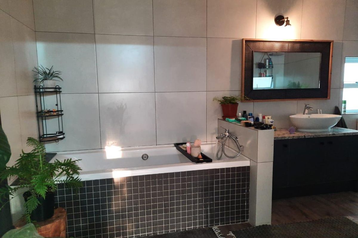 Modern bathroom featuring a built-in bathtub with dark mosaic tiling, a vanity with a vessel sink, and large format wall tiles.