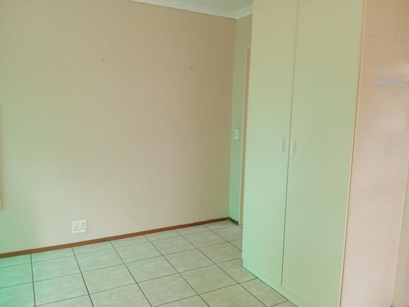 A simple, empty bedroom featuring neutral wall paint, tiled flooring, and a built-in wardrobe.