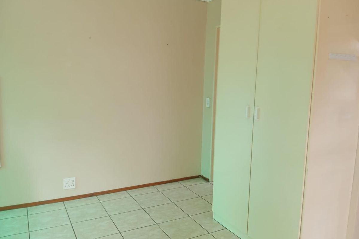 A simple, empty bedroom featuring neutral wall paint, tiled flooring, and a built-in wardrobe.