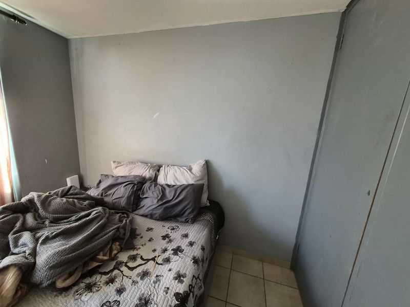 A bedroom featuring tiled flooring and a built-in cupboard, currently requiring minor cosmetic updates to the wall finishes.