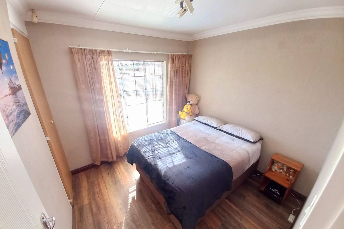 A standard bedroom featuring wood-look laminate flooring, a window with curtain tracks, and built-in door access.
