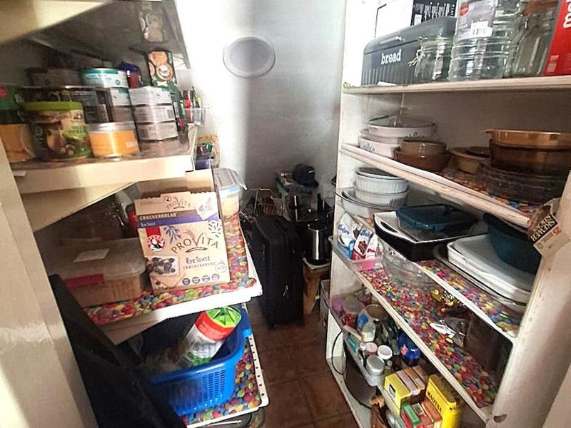 A narrow walk-in pantry or scullery area featuring built-in shelving units and tiled flooring, providing ample storage space for kitchen essentials.