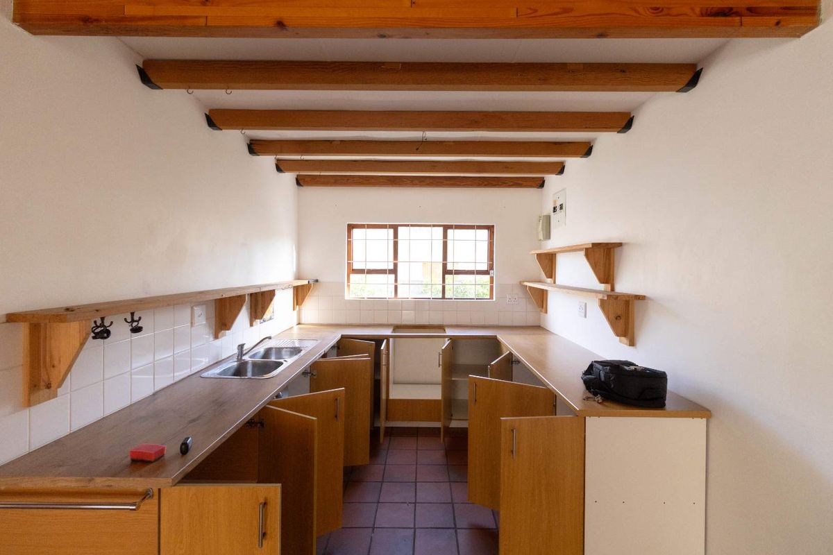 A functional kitchen space featuring exposed timber ceiling beams, laminate countertops, a double bowl sink, and terracotta floor tiles, awaiting modern updates.