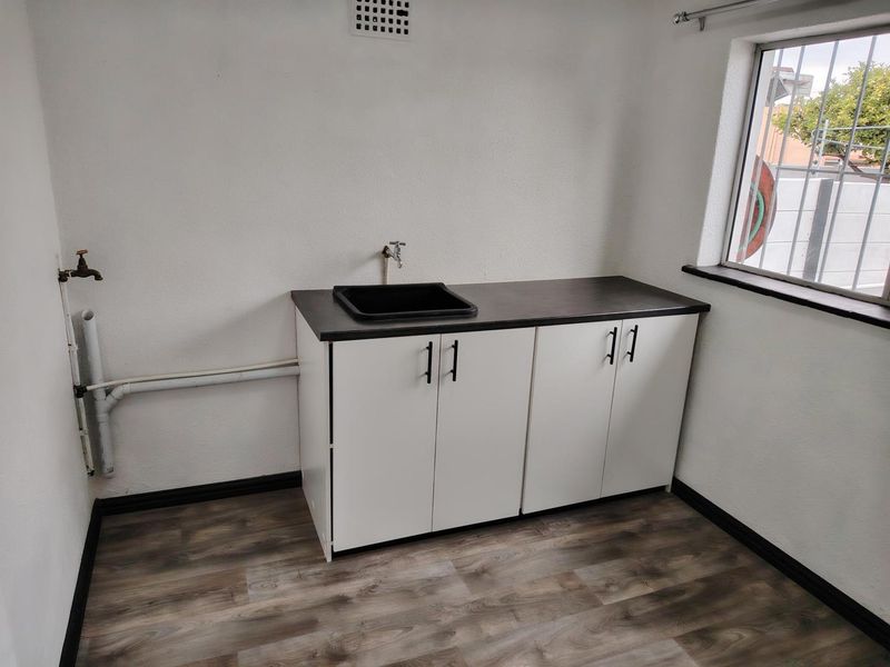 A clean, functional laundry area featuring built-in white cabinetry, a dark laminate countertop with a sink, and durable wood-look laminate flooring.