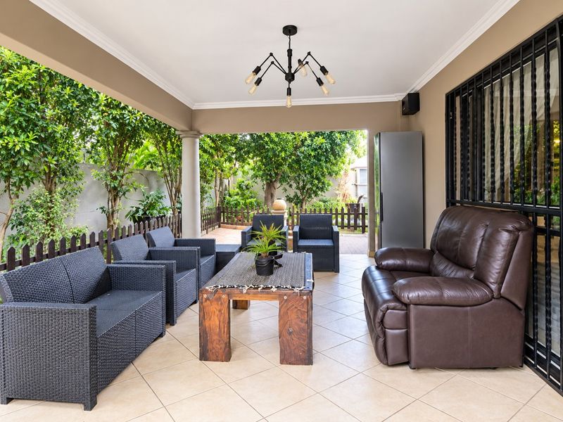 A spacious covered patio featuring tiled flooring, a modern chandelier, and direct access to a private garden area.