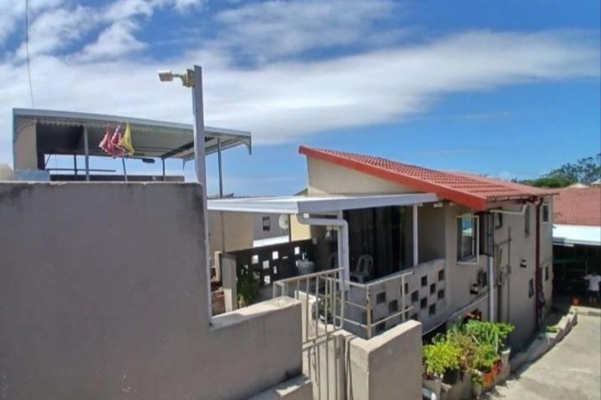 Rear exterior view of the property featuring a covered patio area, tiled roof, and concrete boundary walls with security gate access.