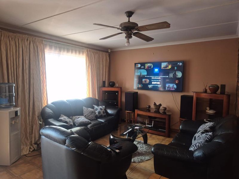 A living room featuring tiled flooring and a ceiling fan, with visible wear on the ceiling panels.