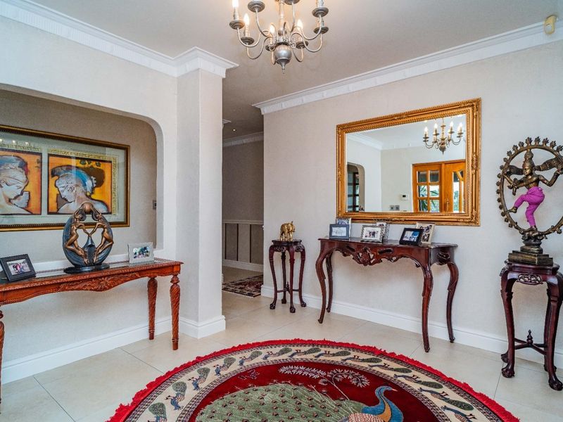 A spacious and elegant entrance hall featuring tiled flooring, decorative crown molding, a central chandelier, and a recessed wall niche.