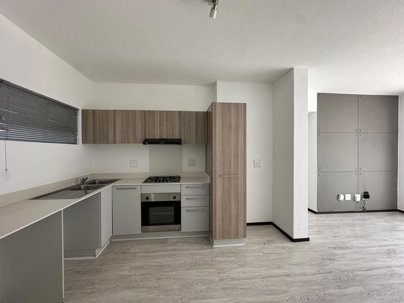 Modern open-plan kitchen and living area featuring wood-look cabinetry, integrated appliances, laminate flooring, and a contemporary grey feature wall.
