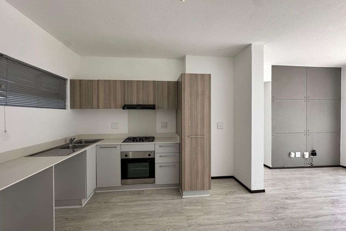 Modern open-plan kitchen and living area featuring wood-look cabinetry, integrated appliances, laminate flooring, and a contemporary grey feature wall.