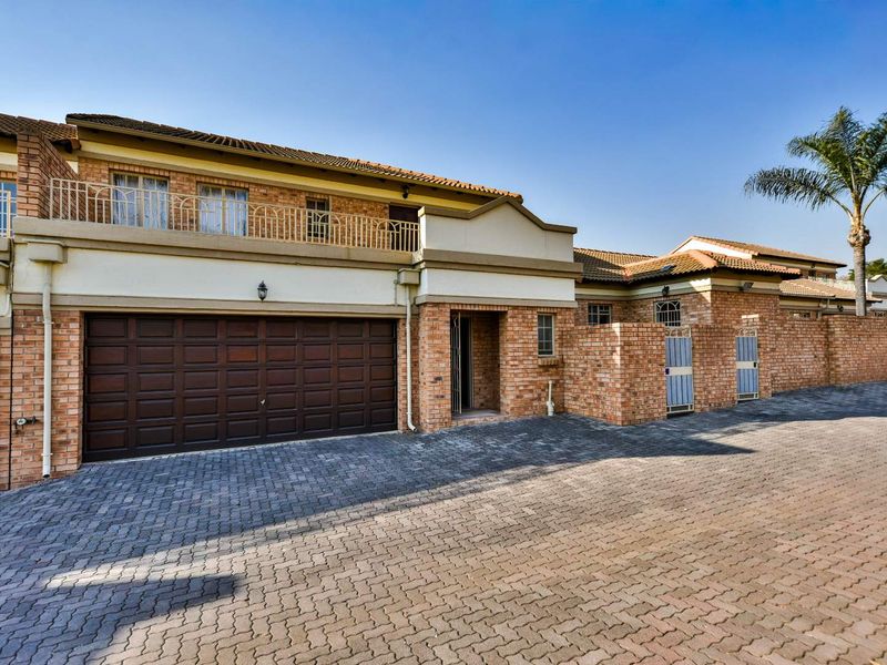Front elevation of a brick townhouse featuring a double garage, paved driveway, and an upper-level balcony with metal railings.