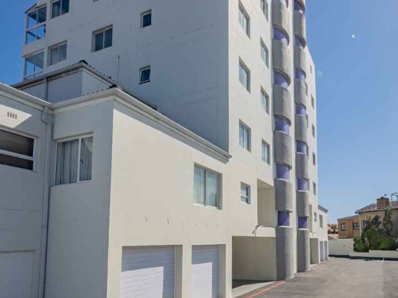Exterior view of a multi-story apartment building featuring a paved driveway and multiple ground-level garage access points.