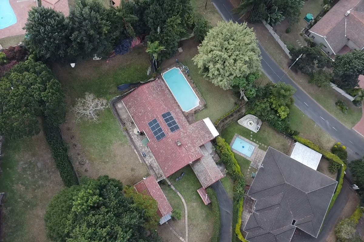 Aerial view of the property featuring a tiled roof, solar panels, a swimming pool, and surrounding garden space within a residential neighborhood.