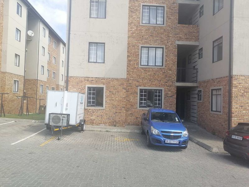 Exterior view of a multi-story townhouse complex featuring face brick facade, paved parking area, and allocated parking bays.
