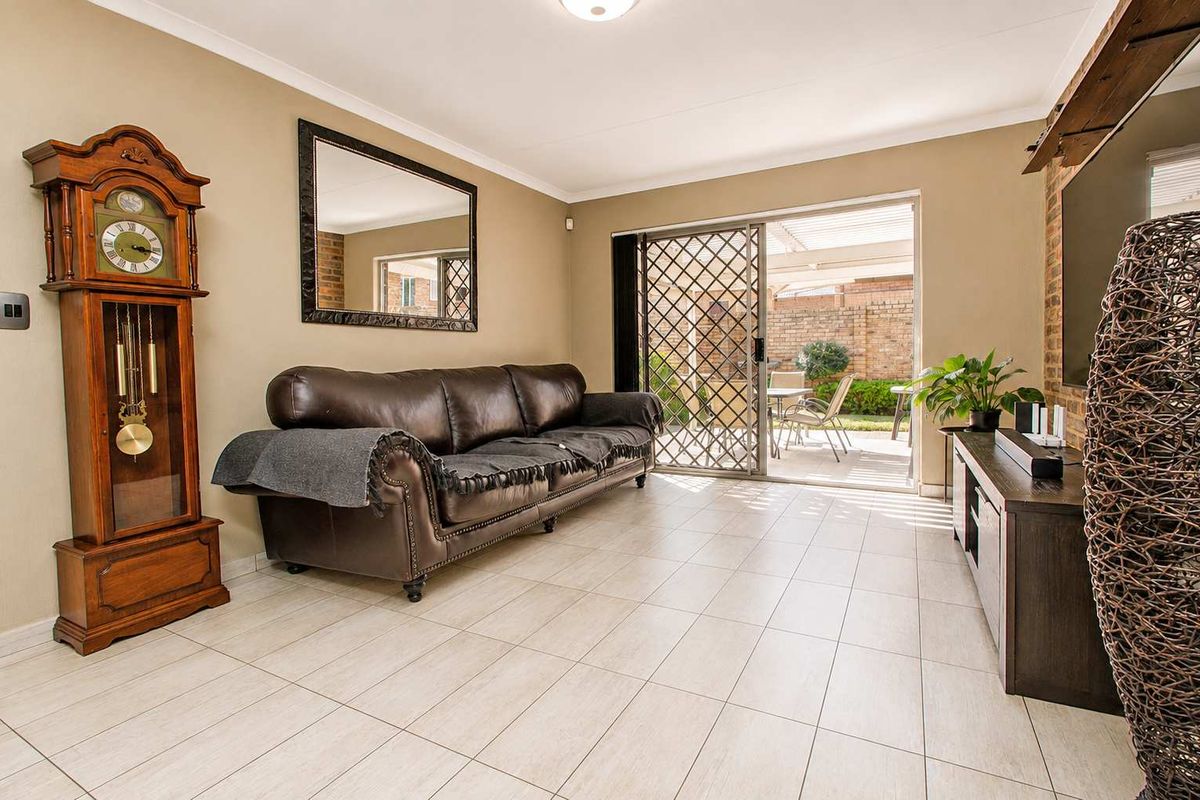 A well-maintained living room featuring neutral tiled flooring, coved ceilings, and a sliding glass door providing direct access to the outdoor patio area.