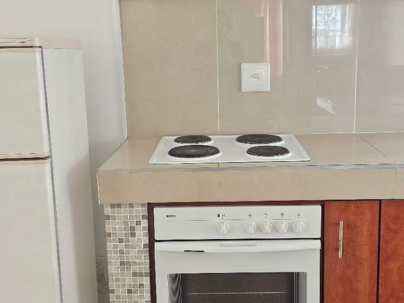 A functional kitchen area featuring built-in cabinetry, a Bosch oven, electric hob, and an extractor fan with decorative tiled splashback.