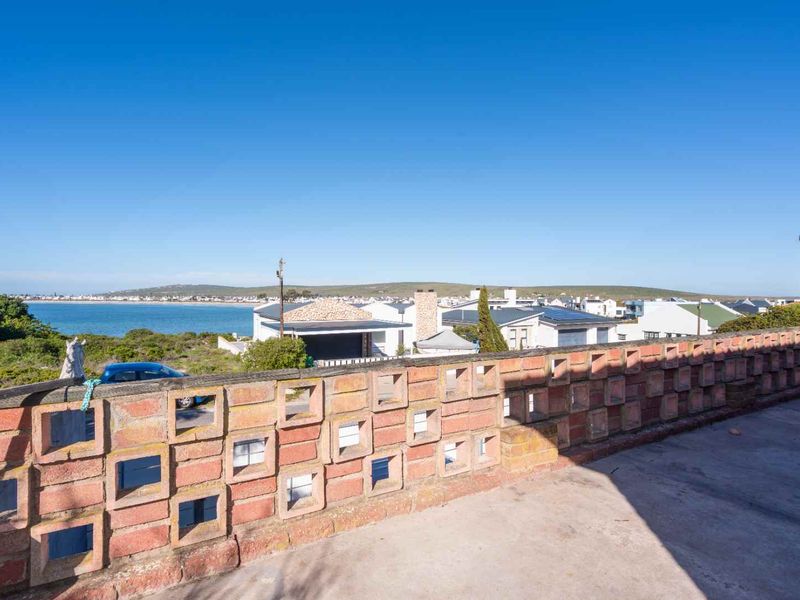 An elevated balcony featuring a decorative brick breeze block balustrade and concrete flooring, offering expansive coastal and neighbourhood views.
