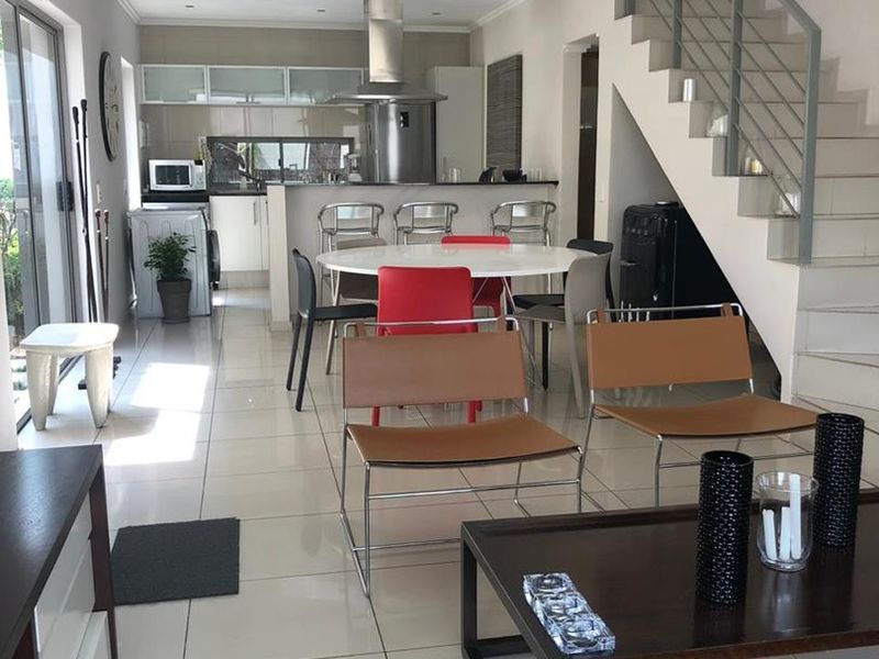 Spacious open-plan living and kitchen area featuring modern tiled floors, a sleek staircase, and direct access to outdoor space through sliding glass doors.