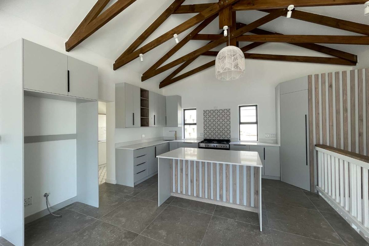 Modern open-plan kitchen featuring light grey cabinetry, stone countertops, a central island, and exposed timber roof trusses.