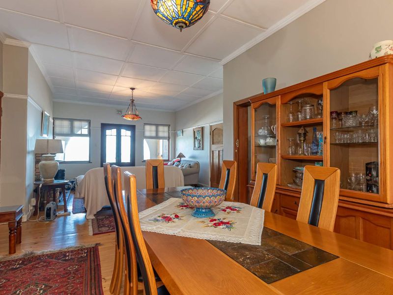 Spacious dining room featuring timber flooring, a tiled ceiling, and classic picture rails, flowing into an adjacent living area.