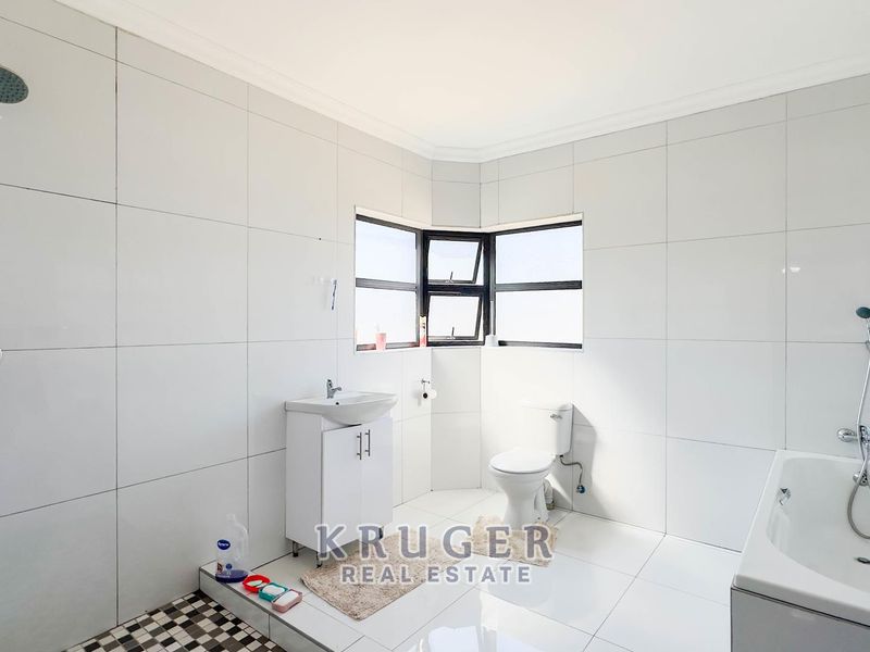 A bright, tiled bathroom featuring a shower, bathtub, vanity basin, and toilet with large format wall tiles.