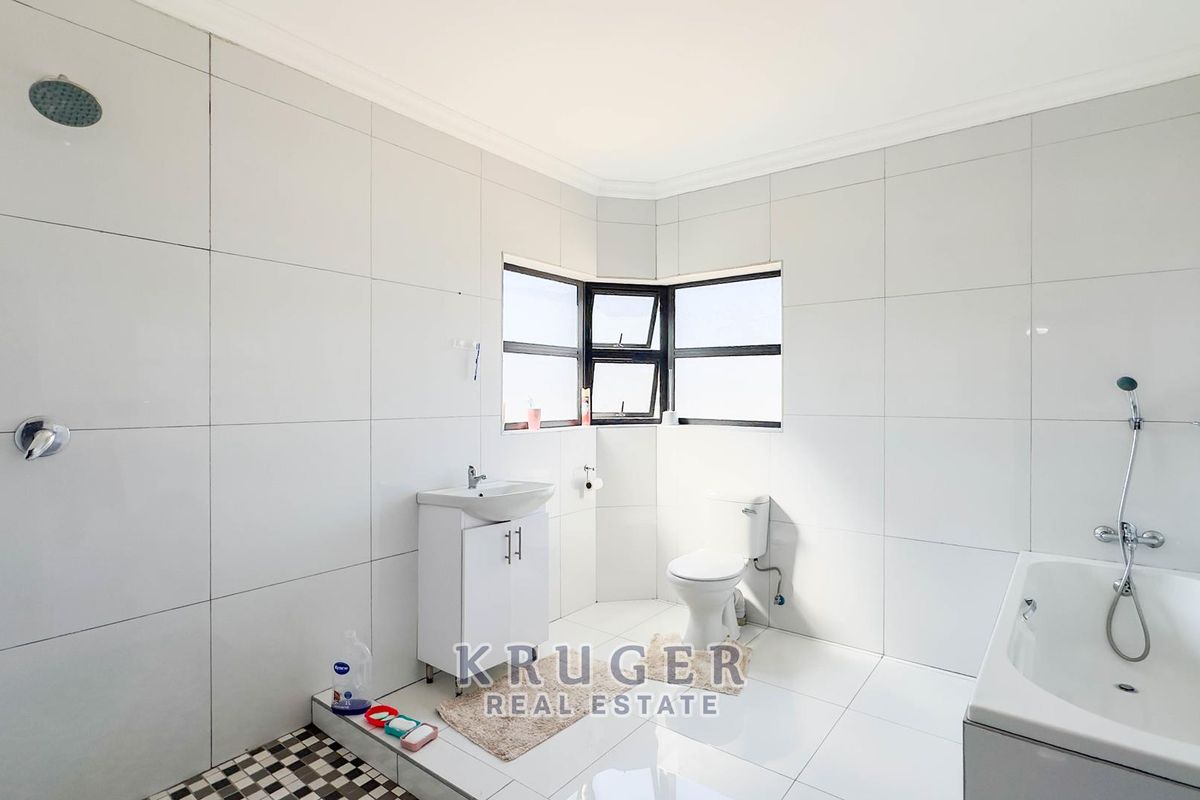 A bright, tiled bathroom featuring a shower, bathtub, vanity basin, and toilet with large format wall tiles.