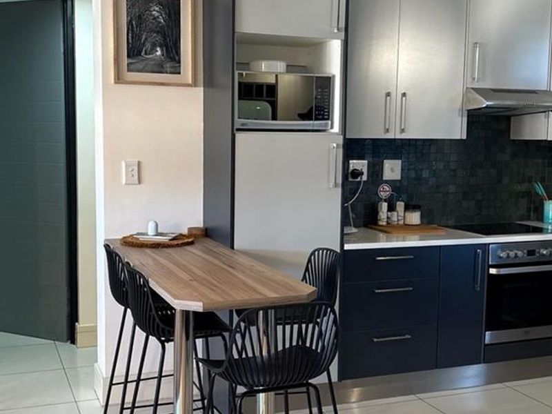 Modern kitchen featuring two-tone cabinetry, built-in appliances, mosaic tile backsplash, and polished floor tiles with an integrated breakfast bar.