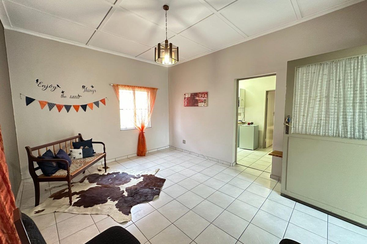 A bright living room featuring tiled flooring, a coffered ceiling, and direct access to an adjoining kitchen area.