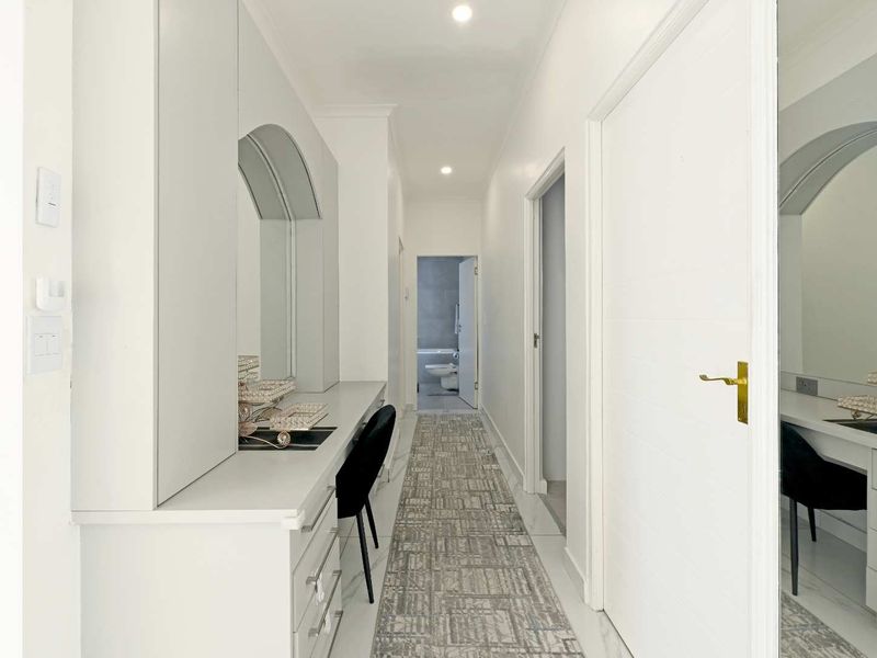 A bright, modern hallway featuring built-in vanity cabinetry with integrated mirrors, recessed lighting, and clean tiled flooring leading towards a bathroom.
