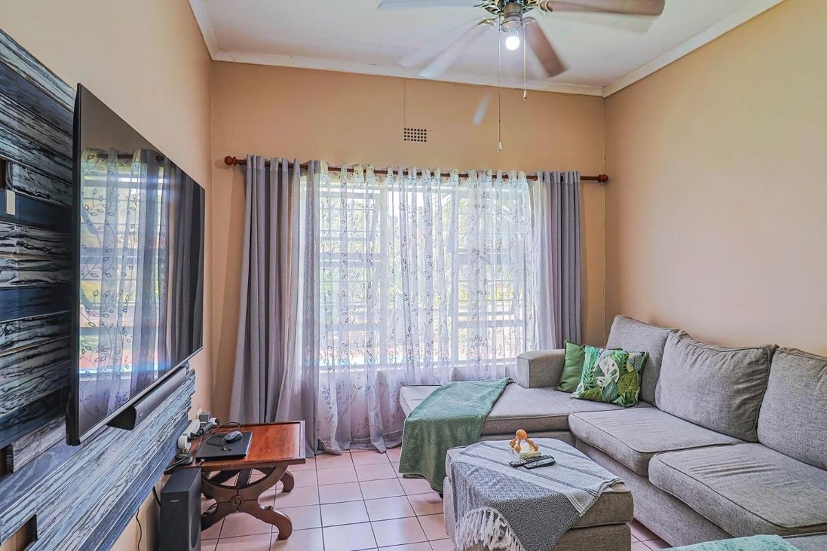 A cozy living room featuring tiled flooring, a ceiling fan, and a large window with curtain treatments, providing a comfortable and functional living space.