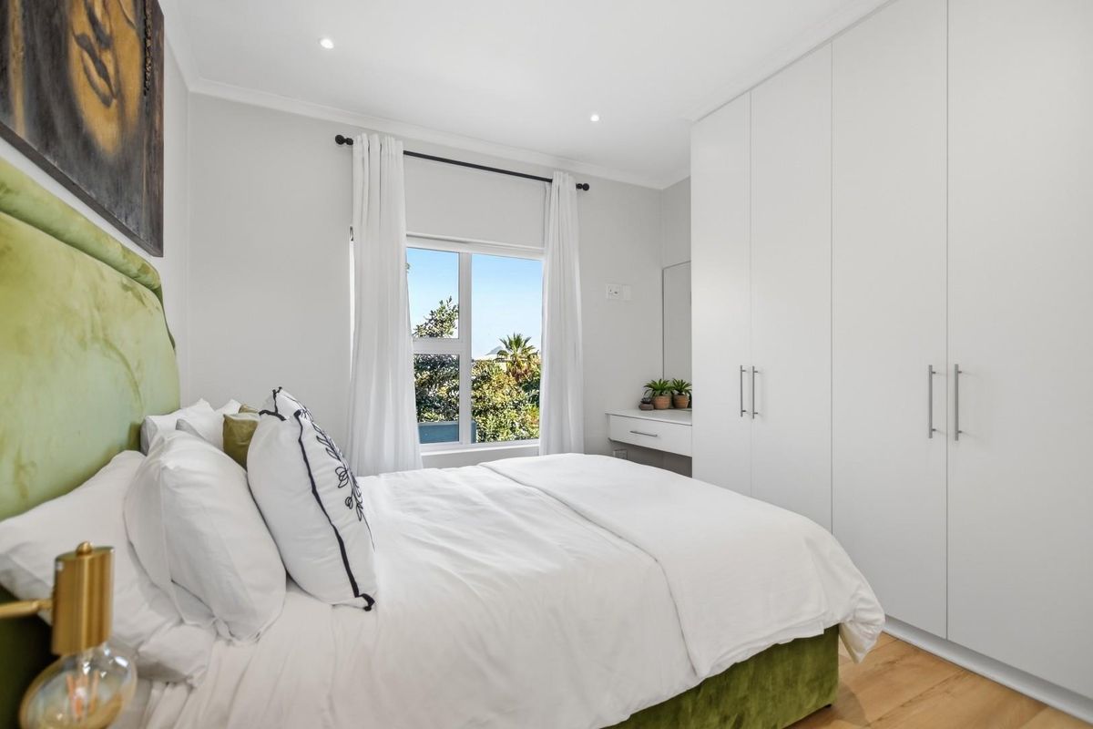 A bright and modern bedroom featuring built-in cupboards, a built-in vanity, laminate flooring, and recessed downlighting with a pleasant outdoor view.