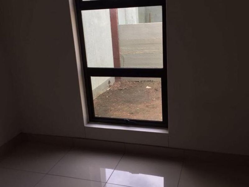 A bright, empty bedroom featuring modern tiled flooring and a large aluminium-framed window overlooking the exterior area.