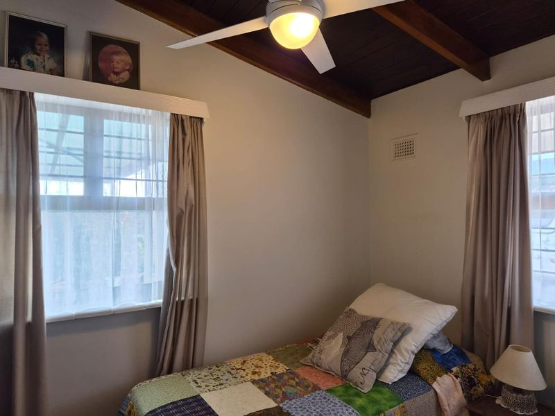 A bedroom featuring a dark timber raked ceiling with exposed beams, a central ceiling fan, and dual windows with neutral curtains.