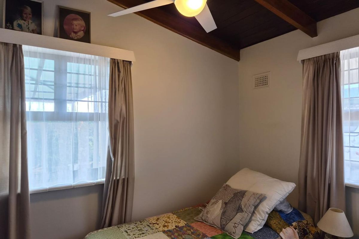 A bedroom featuring a dark timber raked ceiling with exposed beams, a central ceiling fan, and dual windows with neutral curtains.