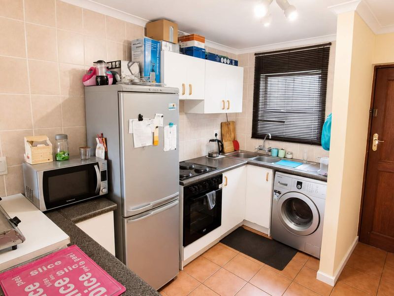Compact kitchen featuring built-in cabinetry, tiled backsplash, electric hob, oven, and integrated plumbing for laundry appliances.