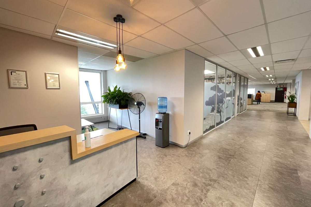 Modern office reception area featuring a built-in desk, glass partition walls, suspended ceiling with recessed lighting, and durable tiled flooring.