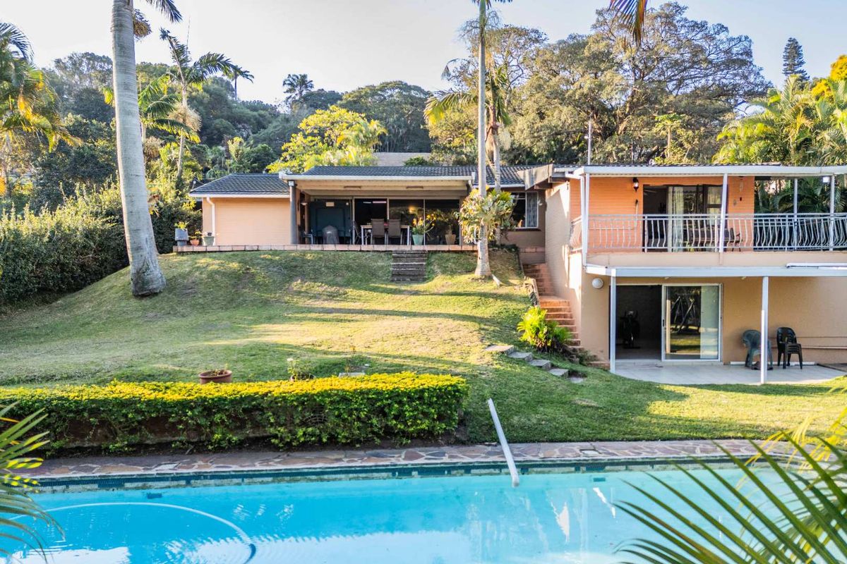 Rear view of the house featuring a swimming pool, covered patio, upper balcony, and landscaped garden area.