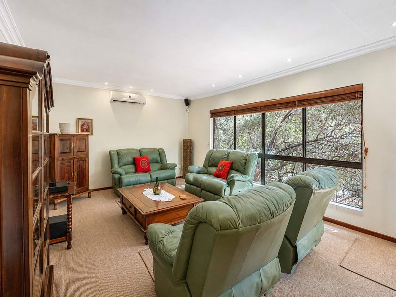 A comfortable living room featuring carpet flooring, recessed downlighting, and a large window providing natural light and garden views.