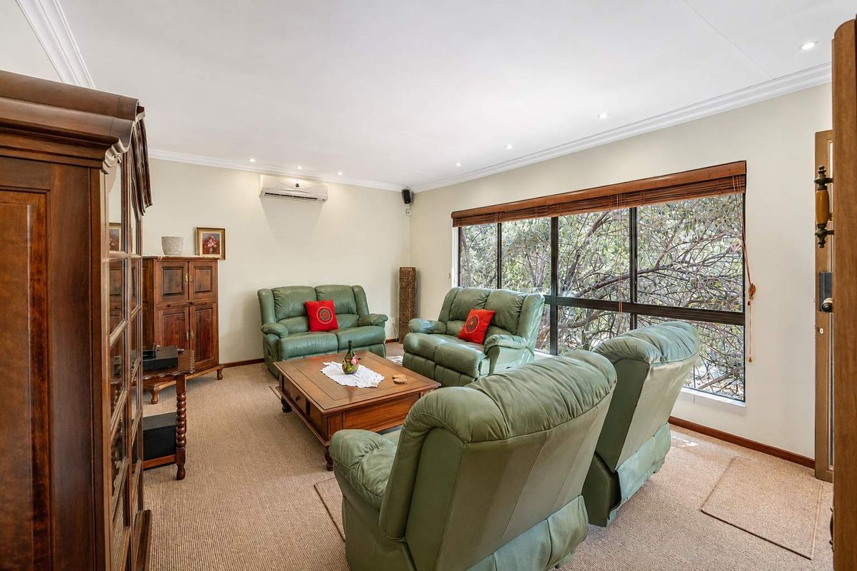 A comfortable living room featuring carpet flooring, recessed downlighting, and a large window providing natural light and garden views.